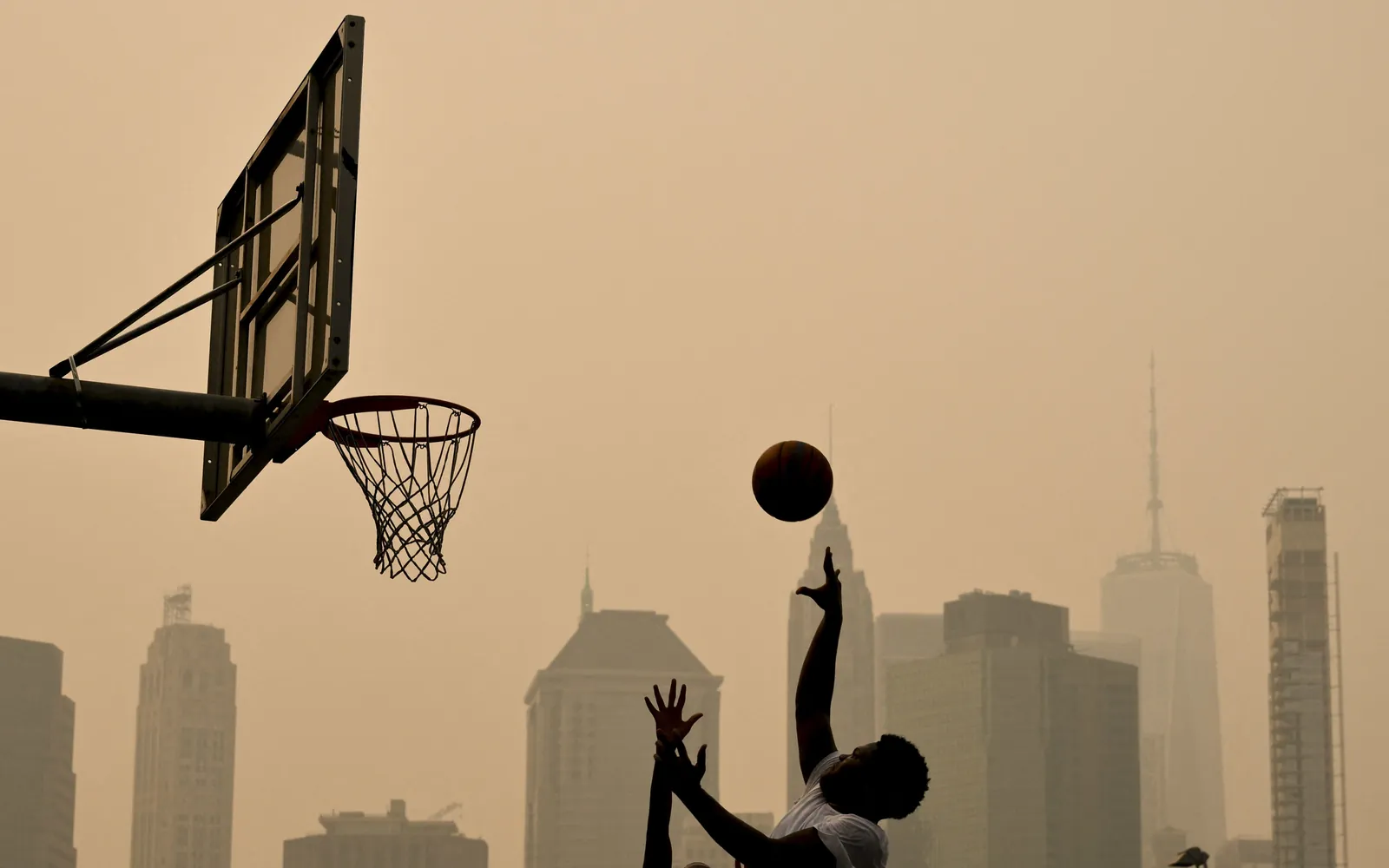 People play basketball as wildfire smoke from Canada causes hazy conditions on July 16, 2026 in New York. Out-of-control wildfires were raging Thursday in the Canadian province of Ontario, prompting evacuations and sending dangerous smoke billowing into the United States where millions of people were exposed to the unhealthy air. US states near the Canadian border including Minnesota, Wisconsin, Michigan and Illinois were particularly choked, as forecasters predicted the Northeast including New York would also see air quality continue to deteriorate. (Photo by ANGELA WEISS / AFP)